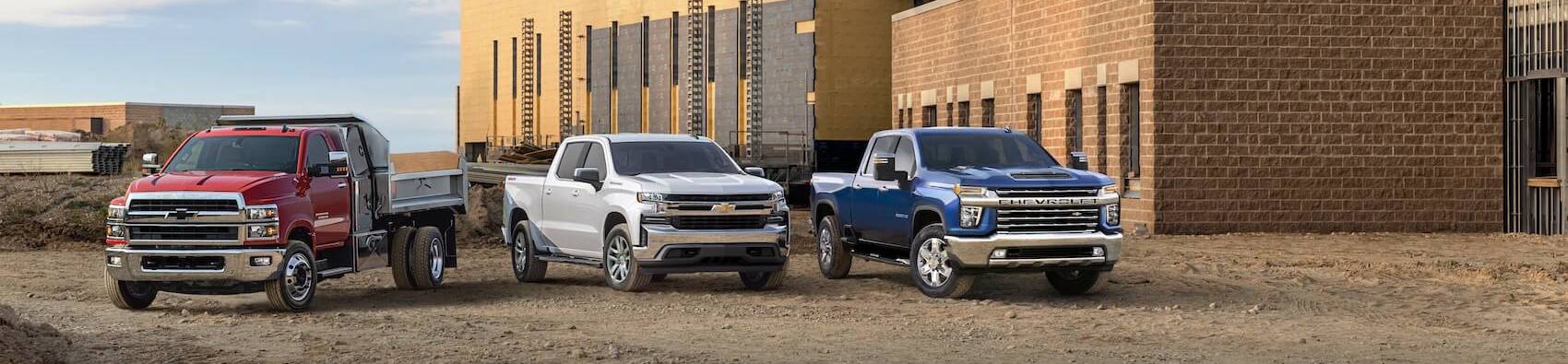Red chevy custom build parked next to a white Chevy Silverado and a blue Chevy Silverado